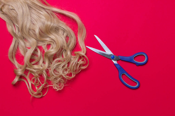 blond hair and scissors on red colored paper background. - Photo, Image
