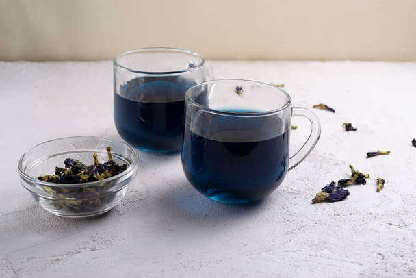 Tè blu Anchan Thai in due tazze di vetro e una ciotola con fiori secchi. Bellissimo colore indaco. Copia spazio. - Foto, immagini