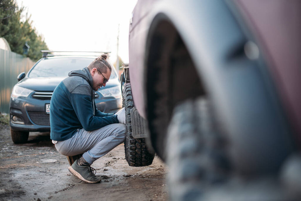 Человек ремонтирует машину, ставит колеса, меняет сезонные шины. Молодой парень сам ремонтирует машину, ставит новые колеса в частный гараж - Фото, изображение