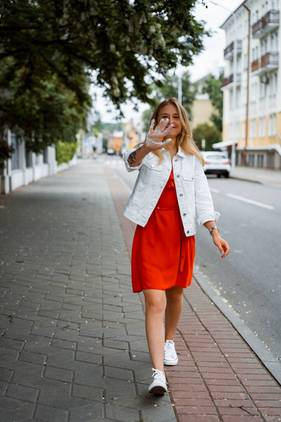 beautiful young woman in a red dress and a white denim jacket, walks around the city a happy smile. Summer. - Fotoğraf, Görsel
