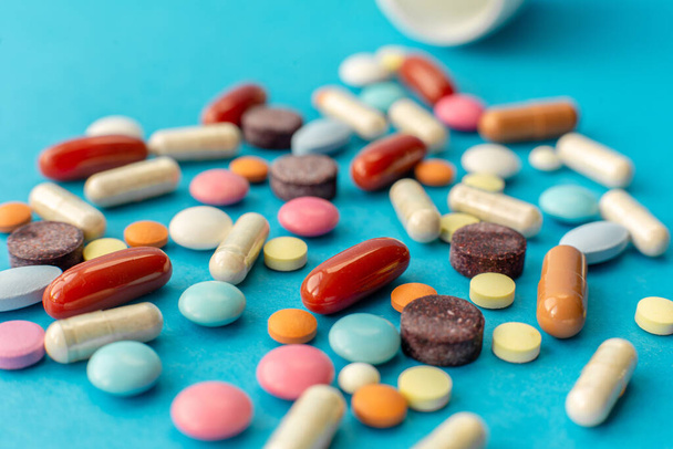 A scattered handful of colored pills on a blue background. Medical concept. - Fotografie, Obrázek