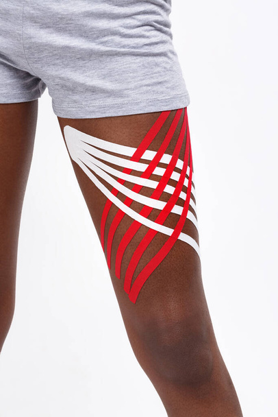 Close up view of kinesiology tape on patient hip.Kinesiology taping. Young female African American athlete.Post traumatic rehabilitation,sport physical therapy,recovery concept,alternative medicine - Foto, afbeelding