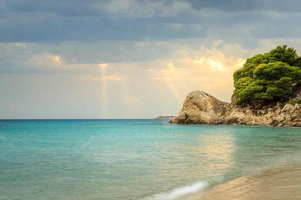 Napsugarak haladnak át a felhők és esik a türkiz tengervíz Koviou strand és gyönyörű sziklák - Fotó, kép