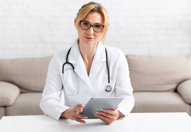 Doktor a on-line lékařská podpora. Atraktivní dospělá lékařka v bílém plášti s tabletou - Fotografie, Obrázek
