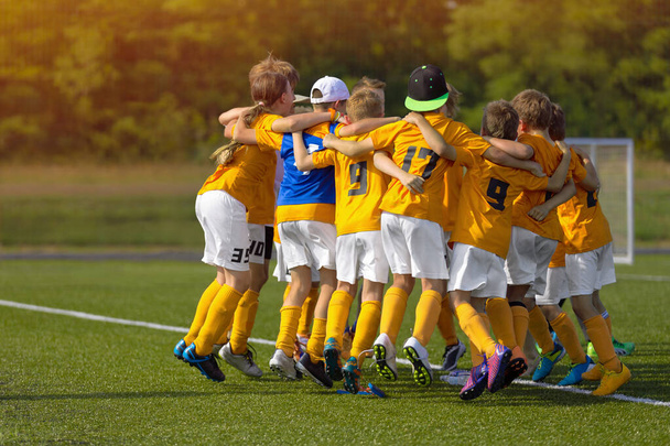 Group of young soccer players celebrate a goal and winning in a game. Happy kids jumping in a circle after winning football final tournament match. Children in sports team huddling - Photo, Image