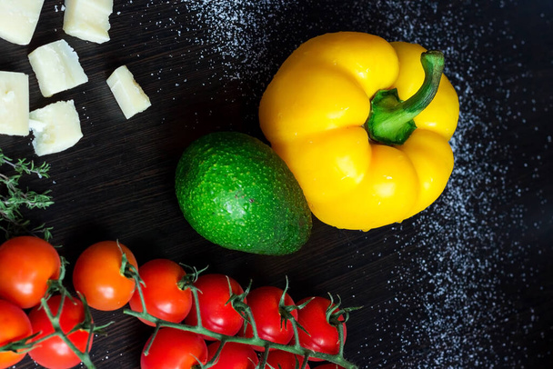 Karanlık arka planda taze organik sebzeler. Ev yapımı salata için malzemeler. Biber, avokado, domates, peynir, kekik, ahşap masada biberiye. Sağlıklı yiyecekler. Sağlıklı yemek.. - Fotoğraf, Görsel