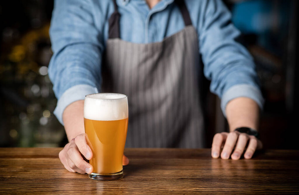 Pití v baru. Barman dává sklenici lehkého piva s pěnou - Fotografie, Obrázek