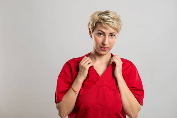 Portrait de jeune infirmière attrayante organisant chemise sur fond gris avec espace de copie publicitaire - Photo, image