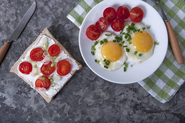 Ένα ορεκτικό πρωινό με τηγανητά αυγά, ψωμί, ντοματίνια και τυρί. Τηγανητά αυγά για πρωινό. Σάντουιτς με τυρί και ντοματίνια. - Φωτογραφία, εικόνα