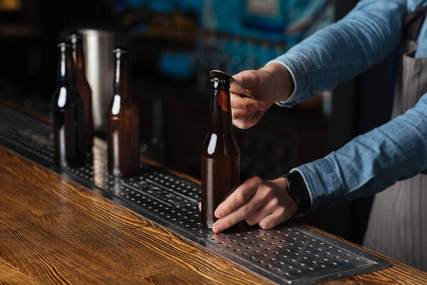 Cold drink for clients. Barman open bottle of beer on wooden bar - Photo, Image
