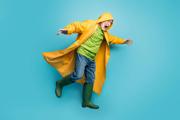 Full length body size view of nice grey-haired man wearing long yellow topcoat balancing on slippery way cyclone hurricane bad weather isolated on bright vivid shine vibrant blue color background - Fotografie, Obrázek