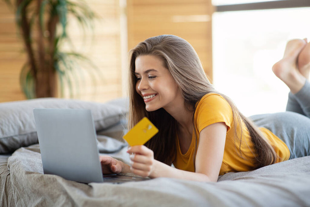 Piękna dziewczyna z laptopa i karty kredytowej zakupy online na łóżku w domu - Zdjęcie, obraz