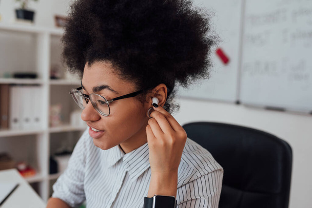 Close up portrait of afro american woman, female teacher adjusting wireless headphones while giving online class through webcam at home - Fotó, kép