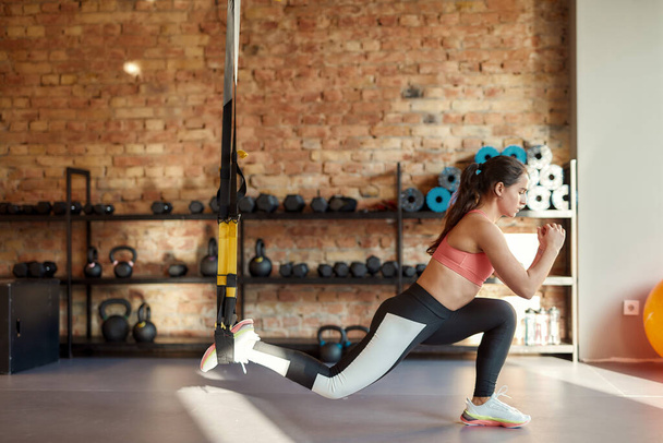 Sportovní mladá žena protahuje své tělo pomocí fitness popruhy v posilovně. Sport, zdravý životní styl koncept - Fotografie, Obrázek