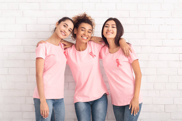 Χαρούμενες γυναίκες σε ροζ καρκίνο του μαστού T-Shirts Αγκαλιάζοντας κοντά στον τοίχο - Φωτογραφία, εικόνα