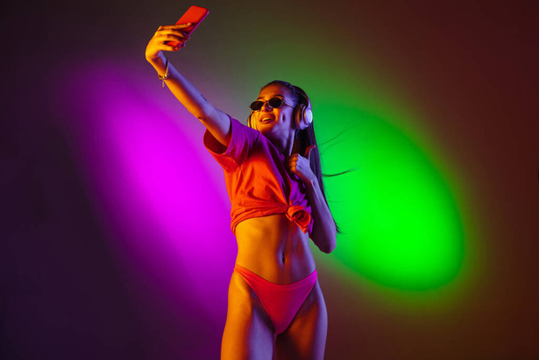 Beautiful seductive girl in fashionable swimsuit on disco bicolored neon studio background in neon light. Summer, resort, fashion and weekend concept - Valokuva, kuva