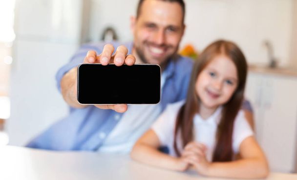 父と娘がキッチンに座っているスマートフォンのブランク画面を表示 - 写真・画像