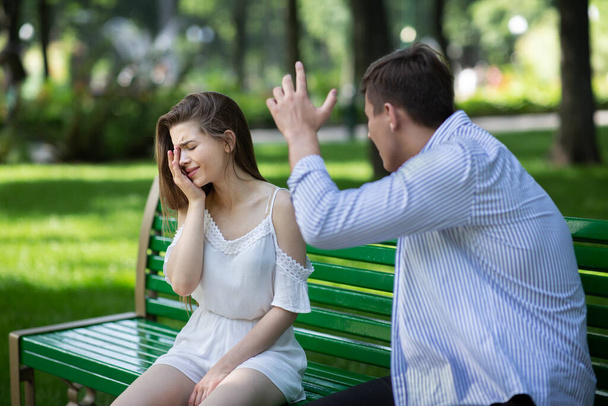 Domestic violence. Angry husband trying to beat his crying wife at park - Photo, Image
