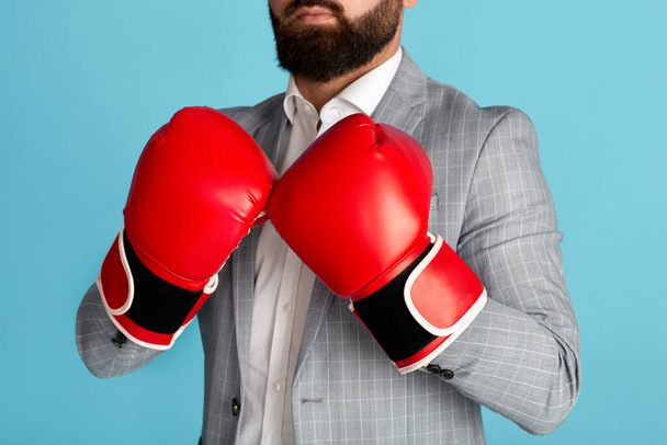 Business competition. Unrecognizable entrepreneur in boxing gloves on blue background, closeup - Photo, Image