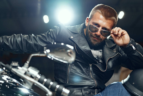 Portrait of bearded man motocyclist in dark sunglasses on dark background - Foto, immagini