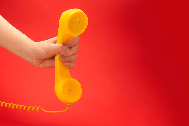 Żółty telefon na czerwonym tle w dłoni kobiety. Przestrzeń kopiowania. - Zdjęcie, obraz