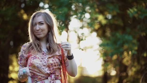 Beautiful young woman wearing bohostyle clothes posing in the rays of the evening sun, sunset. Boho style fashion, female wearing silver jewelry having fun in park outdoors. - Filmagem, Vídeo