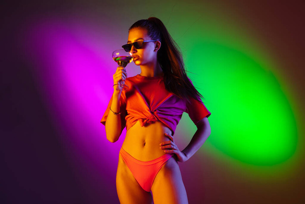 Beautiful seductive girl in fashionable swimsuit on disco bicolored neon studio background in neon light. Summer, resort, fashion and weekend concept - Fotografie, Obrázek
