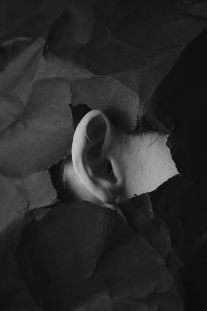 Womans ear in hole in black crumpled paper background, black and white concept photography for blog or poster - Foto, Imagem