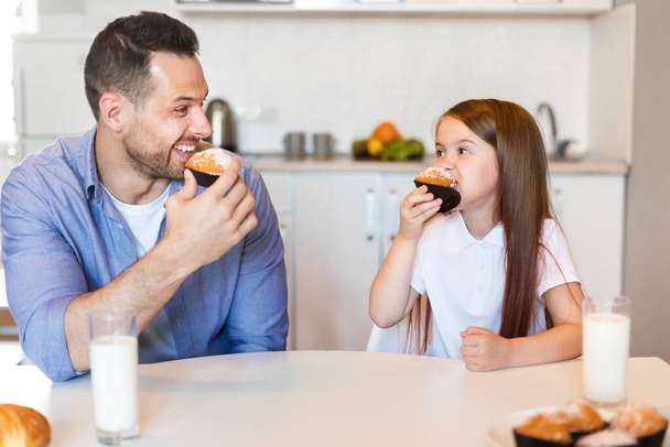 Το κοριτσάκι και ο πατέρας της τρώνε κεκάκια στην κουζίνα. - Φωτογραφία, εικόνα