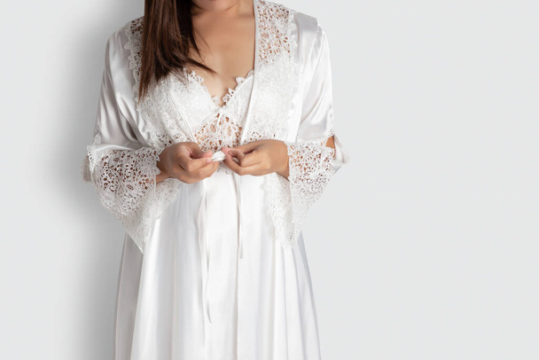 Women put on white sexy nightgown & long sleeve satin robe with floral lace, A girl trying on new white nightwear for sleep. Light gray empty space on right side - Фото, изображение
