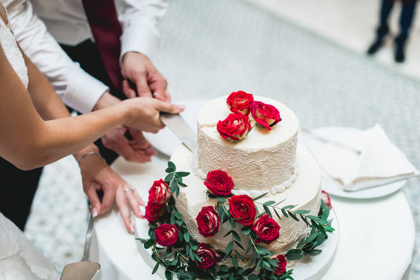 Trauung. Braut und Bräutigam machen ihren ersten Fall zusammen, schneiden die wunderschöne Hochzeitstorte an, die mit Blumen dekoriert ist - Foto, Bild