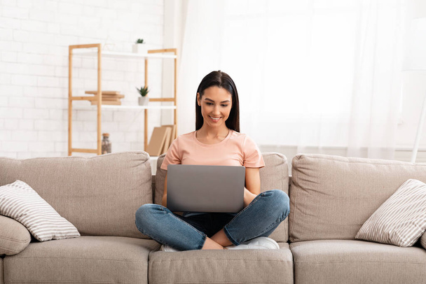 Woman using laptop phone sitting on sofa, free space - Фото, зображення