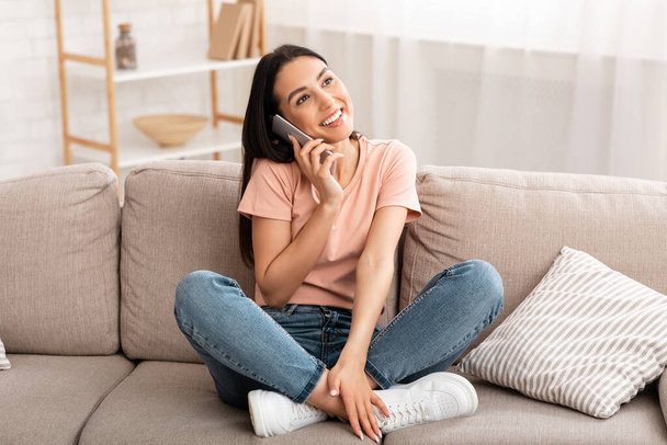 Smiling woman talking on mobile phone sitting on couch - Photo, Image