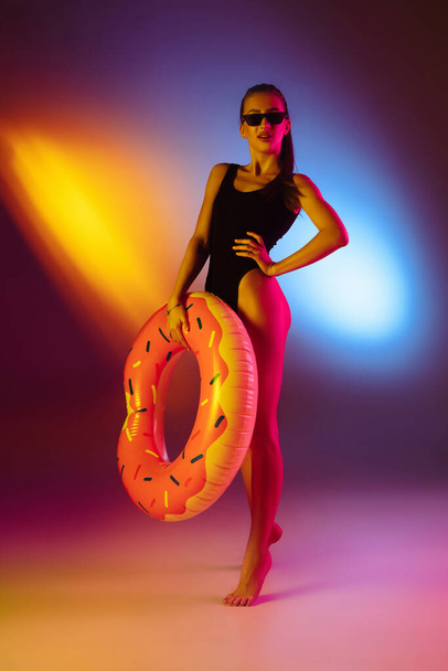 Beautiful seductive girl in fashionable swimsuit on disco bicolored neon studio background in neon light. Summer, resort, fashion and weekend concept - 写真・画像