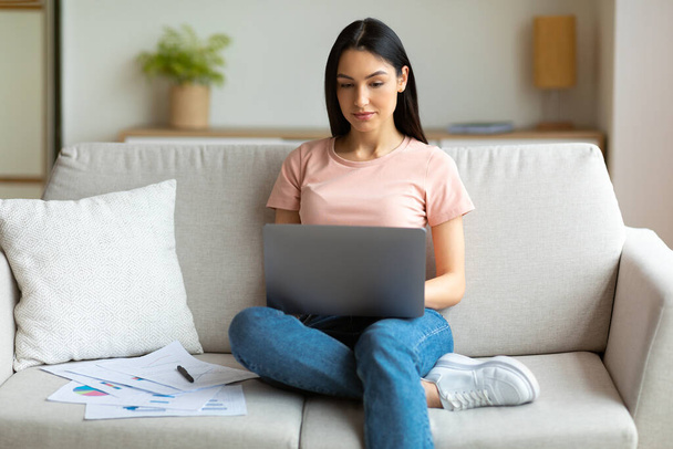 Девушка работает на ноутбуке онлайн сидит на диване дома
 - Фото, изображение