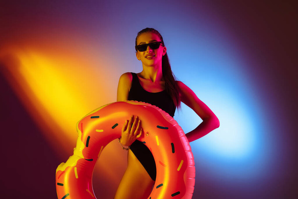 Beautiful seductive girl in fashionable swimsuit on disco bicolored neon studio background in neon light. Summer, resort, fashion and weekend concept - Fotó, kép