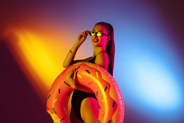 Beautiful seductive girl in fashionable swimsuit on disco bicolored neon studio background in neon light. Summer, resort, fashion and weekend concept - Φωτογραφία, εικόνα