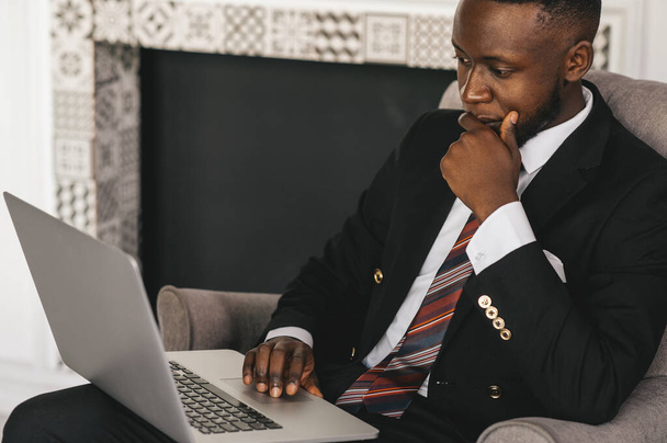 Handsome Afro American businessman in classic suit is using a laptop and smiling while working in modern office - Foto, Bild