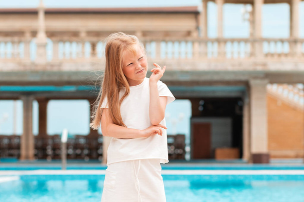 Emoções. O retrato de uma menina está à beira da piscina, com as pernas afastadas, a pensar:
. - Foto, Imagem