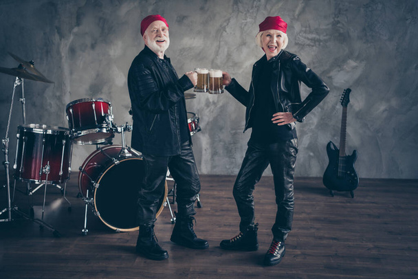 Full size photo of pensioners two people friends lady man rock group drink beer glass drum instruments behind wear stylish rocker leather outfit bandana isolated concrete wall background - Fotoğraf, Görsel