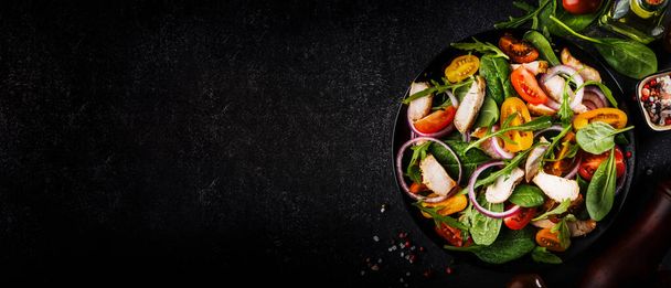 Spring salad with spinach, grilled chicken, cherry tomatoes, arugula, corn salad and red onion. Healthy food concept. Black stone table. Top view. Panoramic banner with place for text - Фото, изображение