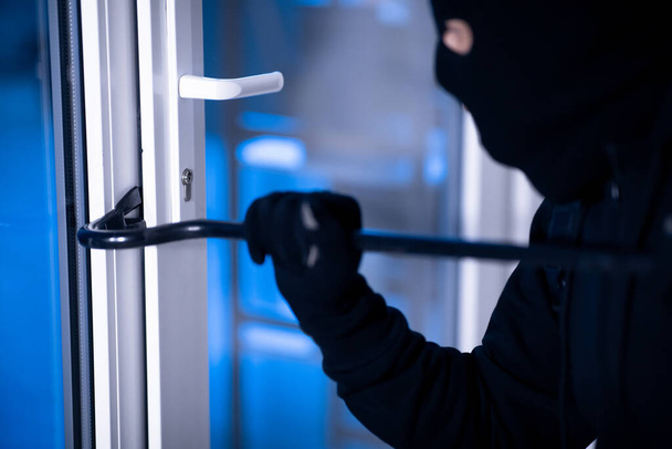 Ladrón en pasamontañas negro rompiendo la puerta con la palanca
 - Foto, imagen