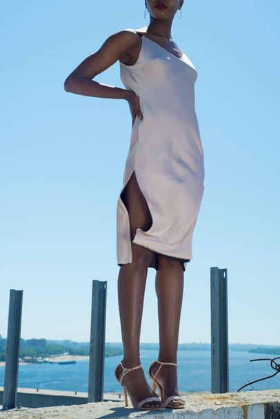 moda africana chica negra en un vestido blanco, modelo posando sobre un fondo de cielo azul. Joven modelo de chica afroamericana en vestido blanco con la espalda abierta posando contra el cielo azul Sexy mujer afroamericana en vestido corto - Foto, imagen