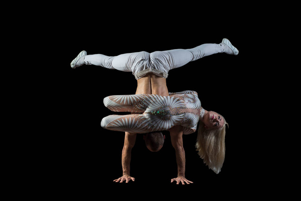 Mężczyzna i kobieta z akrobacją tworzą portret akrobaty faceta z dziewczyną w bieli odizolowaną na czarnym tle. Umiejętności akrobatyczne, taniec sportowy, aktywny tryb życia, wykonywać akrobacje kaskaderskie na podłodze. - Zdjęcie, obraz