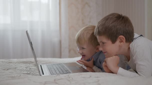 παιδί αρσενικό χρησιμοποιώντας εκπαιδευτική εφαρμογή στον υπολογιστή κάθεται σε καναπέ με μικρό ευτυχισμένο αδελφό να διασκεδάσουν βλέποντας ταινίες animation βίντεο για τα παιδιά - Πλάνα, βίντεο