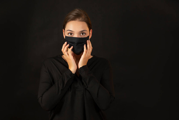 Μελαχρινή νεαρή γυναίκα αγγίζει το πρόσωπό της με προστατευτική μάσκα. - Φωτογραφία, εικόνα