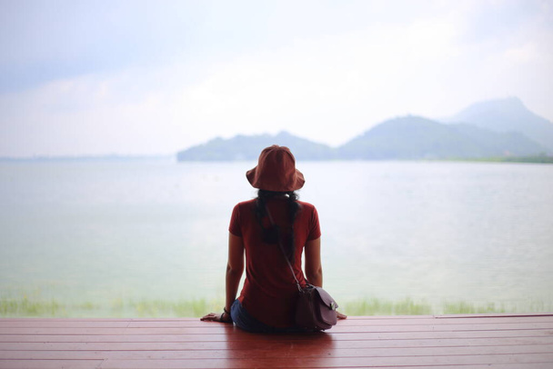 Uma mulher sentada e desfrutando da vista do rio e da montanha
 - Foto, Imagem