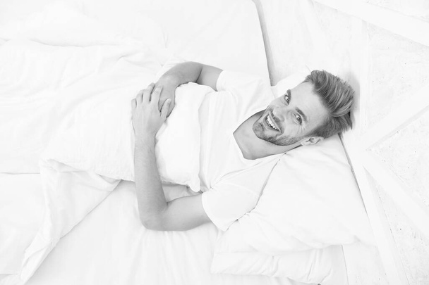 woke up in good mood. man lye in bed. early morning wake up. man rest white bedroom. cosy weekend at home. time to relax. happy guy good morning. male health concept. nice beginning of the day - Fotografie, Obrázek