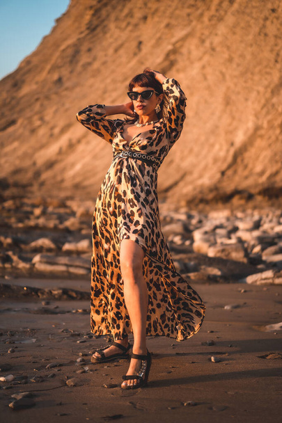 Young woman in leopard dress by the sea at sunset. - 写真・画像