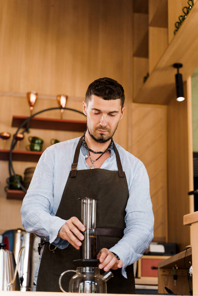 Aeropress kávé és jóképű szakállas barista a kávézóban. Barisa főzni ízletes kávét alternatív főzési módszerrel. Függőleges fotó hirdetéshez a közösségi oldalakon. - Fotó, kép